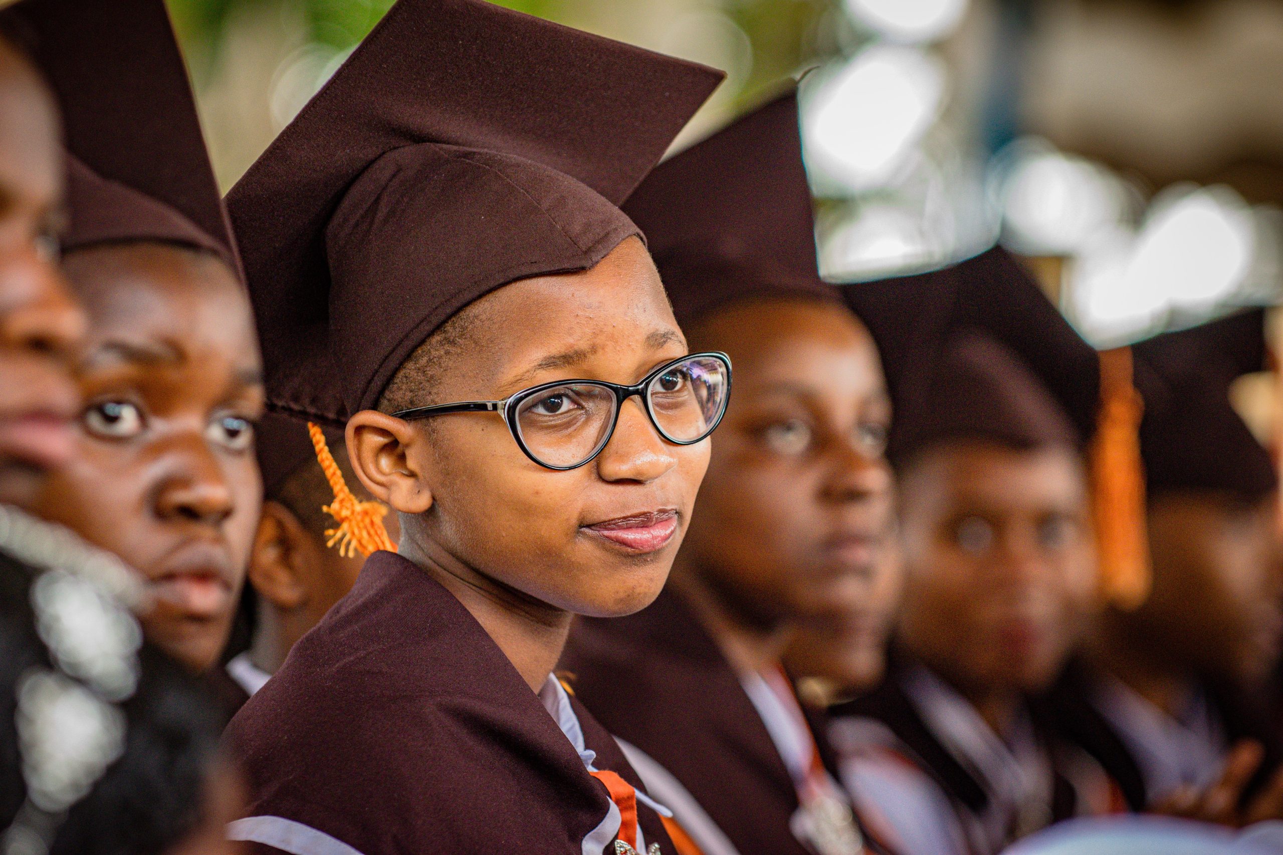 A group of young graduates in caps and gowns attentively participate in a ceremony.